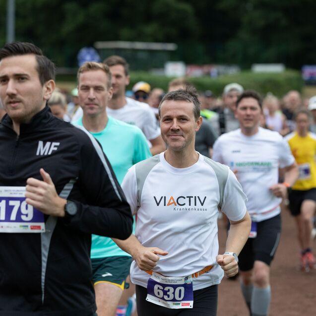 Group of runners participating in a race, focused on the man in a white shirt with "VIACTIV" logo.