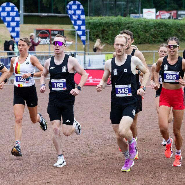 Mehrere Läufer in Sportkleidung nehmen an einem Wettbewerb auf einer Roten Laufbahn teil.