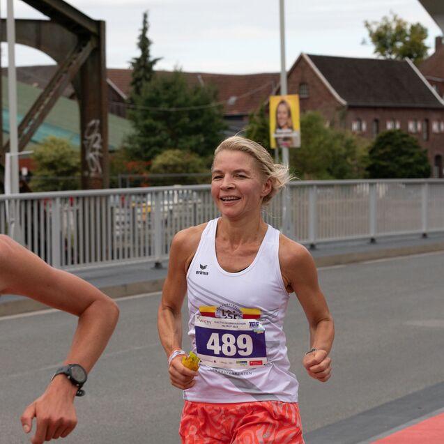 Zwei Frauen laufen bei einem Wettbewerb auf einer Br&uuml;cke; eine Teilnehmerin l&auml;chelt und tr&auml;gt eine Startnummer.