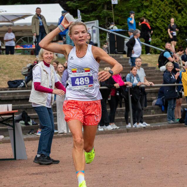 L&auml;uferin mit Startnummer 489 spritzt Wasser &uuml;ber sich w&auml;hrend eines Wettkampfs, Zuschauer applaudieren im Hintergrund.