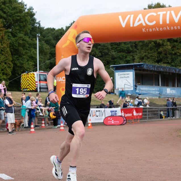 L&auml;ufer mit der Startnummer 195 sprintet unter einem Bogen mit dem Logo &bdquo;VIACTIV&ldquo; und wird von Zuschauern angefeuert.