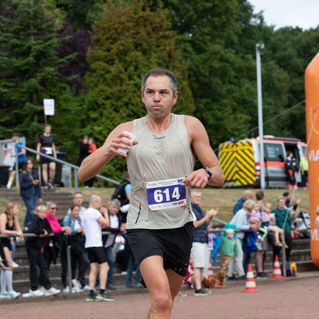 L&auml;ufer mit Startnummer 614, w&auml;hrend er eine Wasserflasche in der Hand h&auml;lt, erreicht das Ziel eines Wettlaufs.