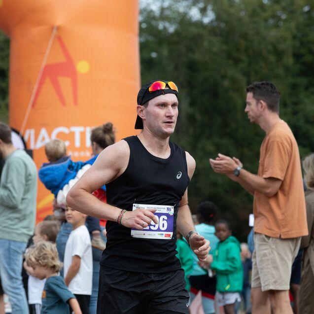 L&auml;ufer in schwarzem Shirt mit Startnummer sprintet an einer orangefarbenen Zielmarkierung vorbei, umgeben von Zuschauern.