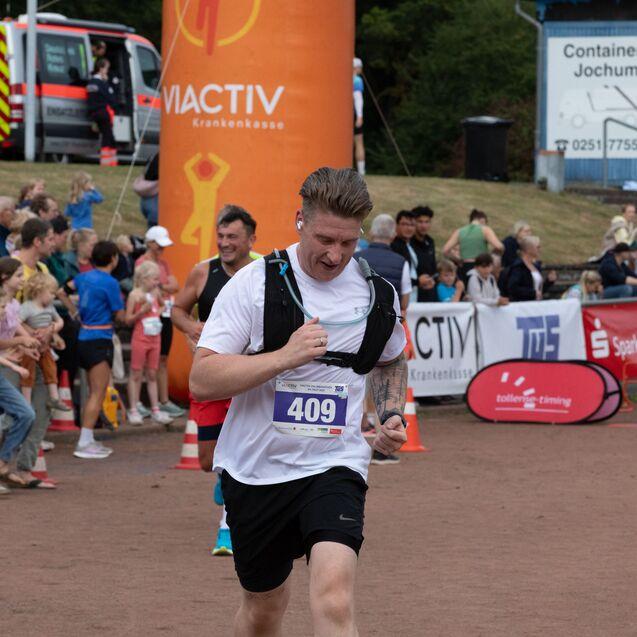 L&auml;ufer mit Startnummer 409 sprintet ins Ziel, umgeben von Zuschauern auf einem Sportgel&auml;nde.