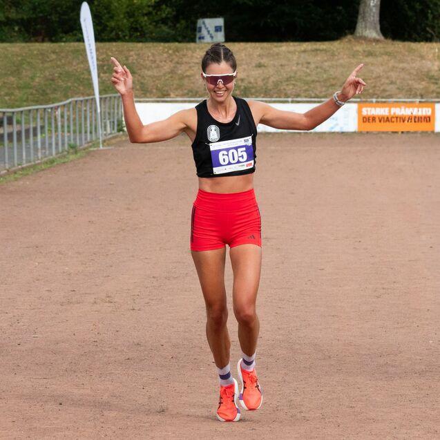 Sportlerin in Sportkleidung mit Startnummer 605 jubelt auf einer Laufbahn nach einem Wettkampf.