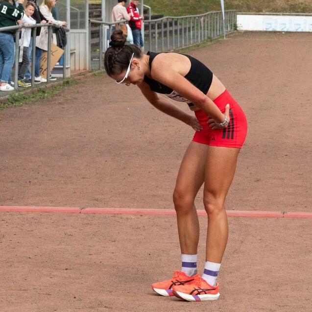 Athletin in Sportkleidung beugt sich m&uuml;de nach dem Wettkampf und fasst sich an die H&uuml;fte auf einer Laufbahn.