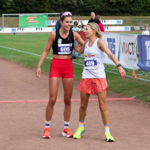 Zwei L&auml;uferinnen umarmen sich nach dem Wettkampf auf einer Laufbahn, im Hintergrund sind Zuschauer und Werbebanner sichtbar.