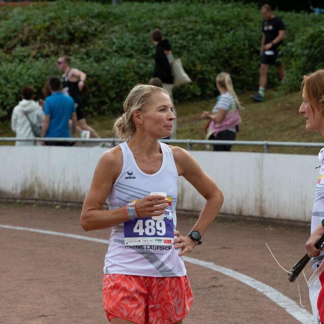 Zwei Frauen unterhalten sich am Rande einer Laufveranstaltung, eine h&auml;lt ein Getr&auml;nk in der Hand.