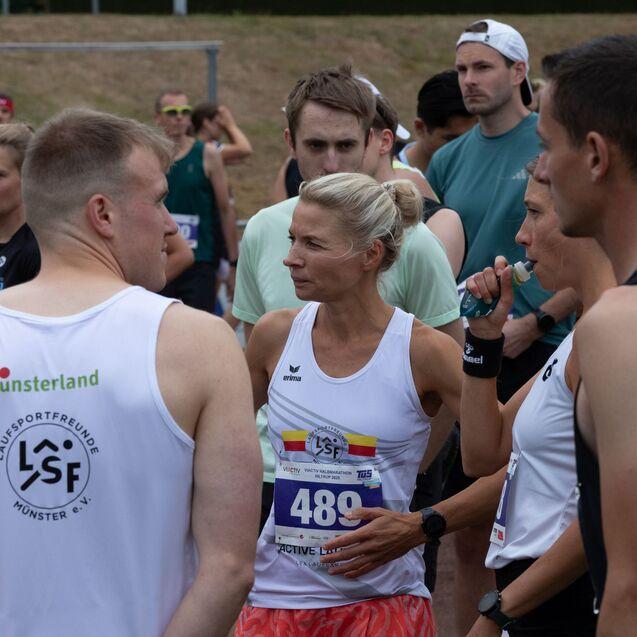 Gruppe von L&auml;ufern in sportlicher Bekleidung, einige mit Startnummern, auf einem Vorbereitungstreffen vor dem Wettkampf.