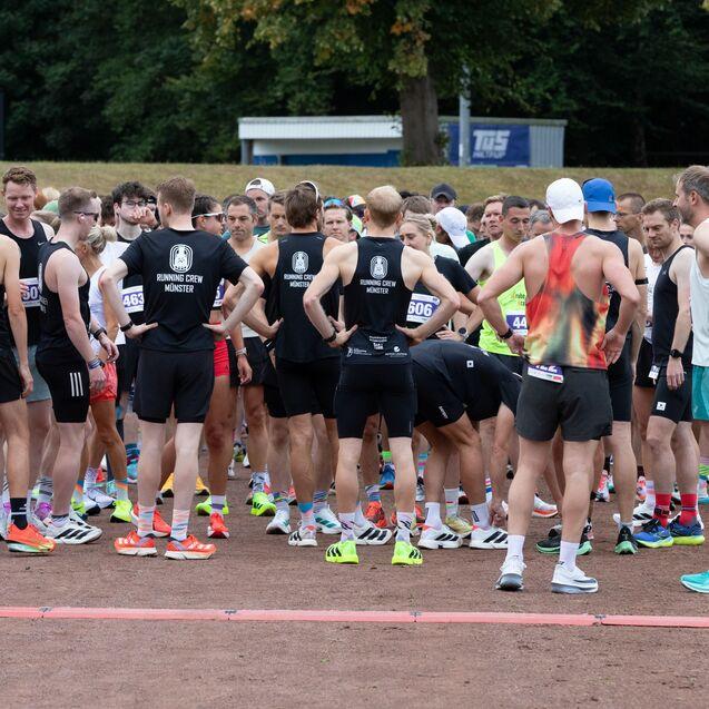 Gruppe von L&auml;ufern in Sportkleidung vor dem Start eines Rennens, einige halten ihre Startnummern in der Hand.
