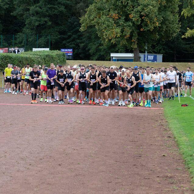 Startline eines Rennens mit zahlreichen L&auml;ufern in Sportkleidung auf einem roten Laufband im Freien.