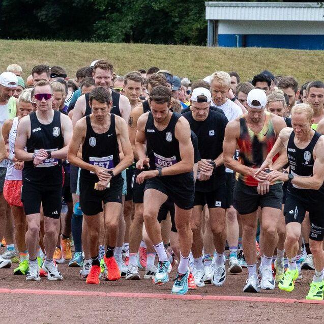 Startaufstellung einer gro&szlig;en Gruppe von L&auml;ufern in Sportkleidung auf einem Laufplatz vor einem Wettkampf.