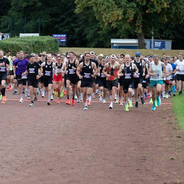 Gruppenschwei&szlig; laufender Sportler in Wettkampfkleidung beim Start eines Lauf-Events auf einem roten Asphaltweg.
