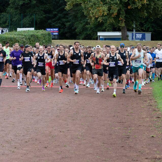 Start einer Laufveranstaltung mit einer Gruppe von L&auml;ufern auf einer roten Rennbahn in einem Sportstadion.