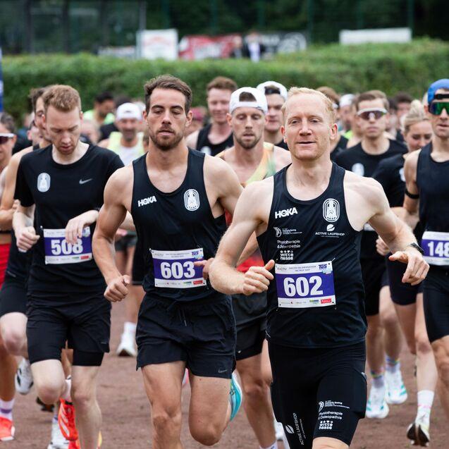 Gruppe von L&auml;ufern in schwarzer Sportkleidung startet beim Wettlauf auf einer Laufbahn.