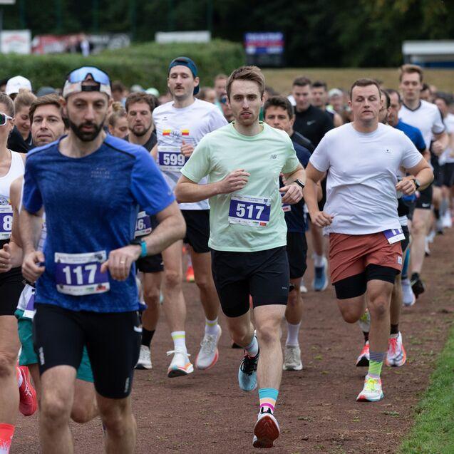 Gruppennahaufnahme von L&auml;ufern beim Wettkampf, zahlreiche Teilnehmer tragen Wettkleidung und Startnummern.