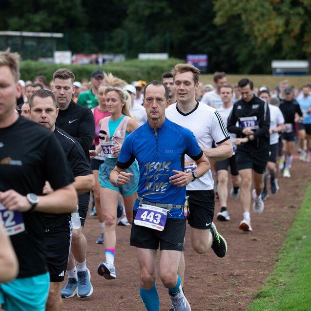 Gruppe von L&auml;ufern auf einer Laufstrecke, die an einem Wettbewerb teilnehmen, mit unterschiedlichen Laufkleidungen und Nummernschildern.