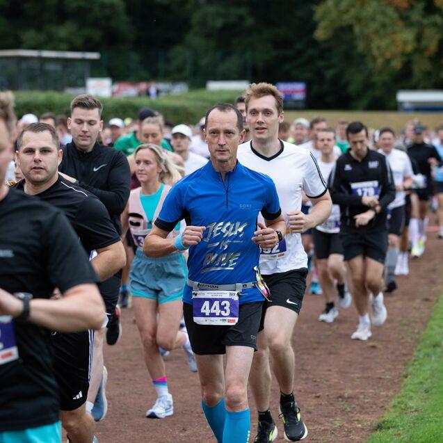 Gruppe von L&auml;ufern in Sportkleidung, die auf einer Laufstrecke an einem Wettkampf teilnehmen.