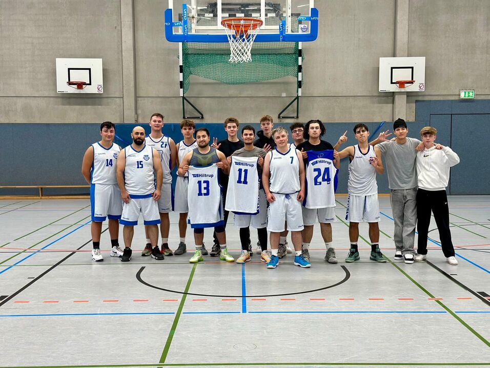 Eine Basketballmannschaft steht in Sportkleidung mit Trikots auf einem Basketballfeld und posiert für das Foto.