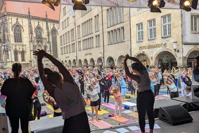 Gruppenyoga-Session im Freien mit Teilnehmern in einem Platz vor einer Kirche, umgeben von Gebäuden.