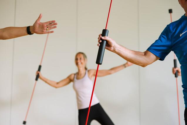Drei Personen führen ein Krafttraining mit roten Widerstandsbändern in einem hellen Raum durch.