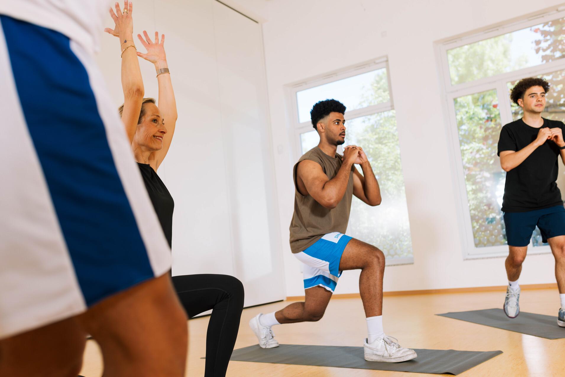 Gruppe von vier Personen beim Krafttraining in einem hellen Fitnessraum mit Matten.