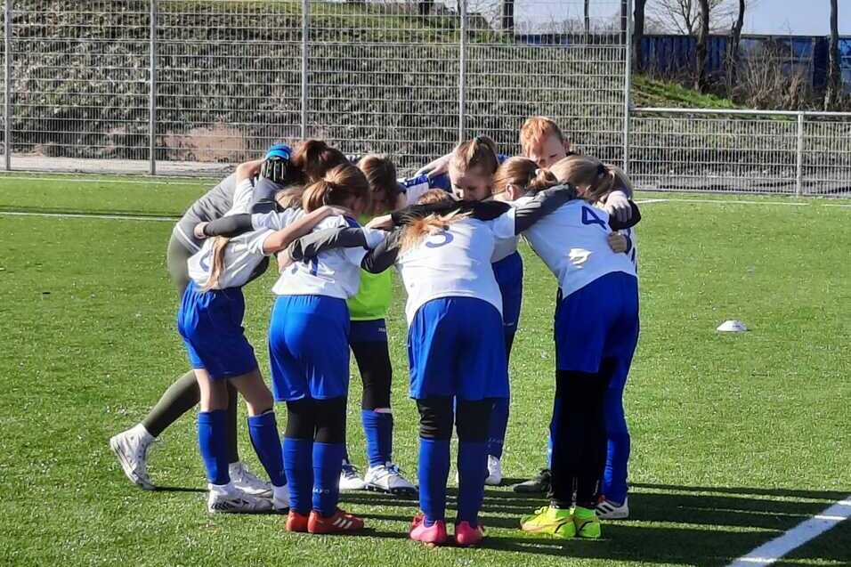 Gruppe von Mädchen in Sportkleidung versammelt sich im Kreis auf einem Fußballplatz, um vor dem Spiel zu besprechen.