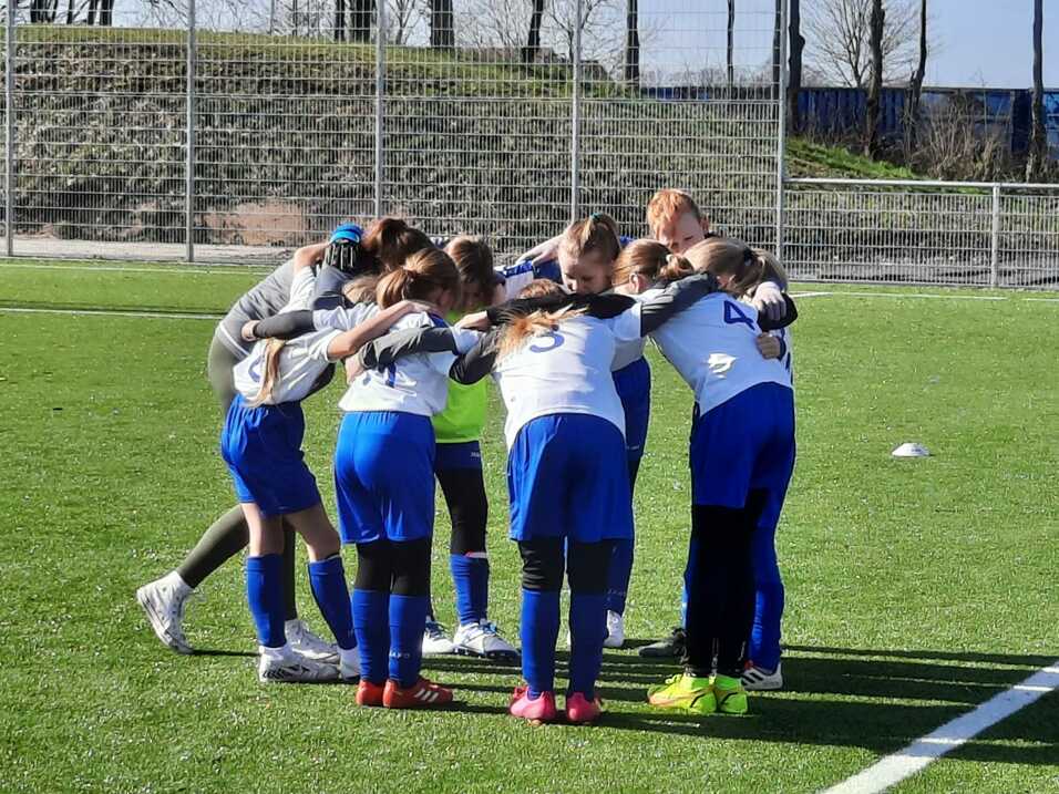 Gruppe von Mädchen in Sportkleidung versammelt sich im Kreis auf einem Fußballplatz, um vor dem Spiel zu besprechen.