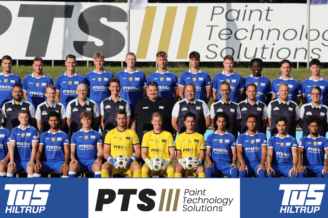 Mannschaftsaufnahme mit Spielern und Trainern in blauen Trikots vor einer Werbebande f&uuml;r PTS Paint Technology Solutions.