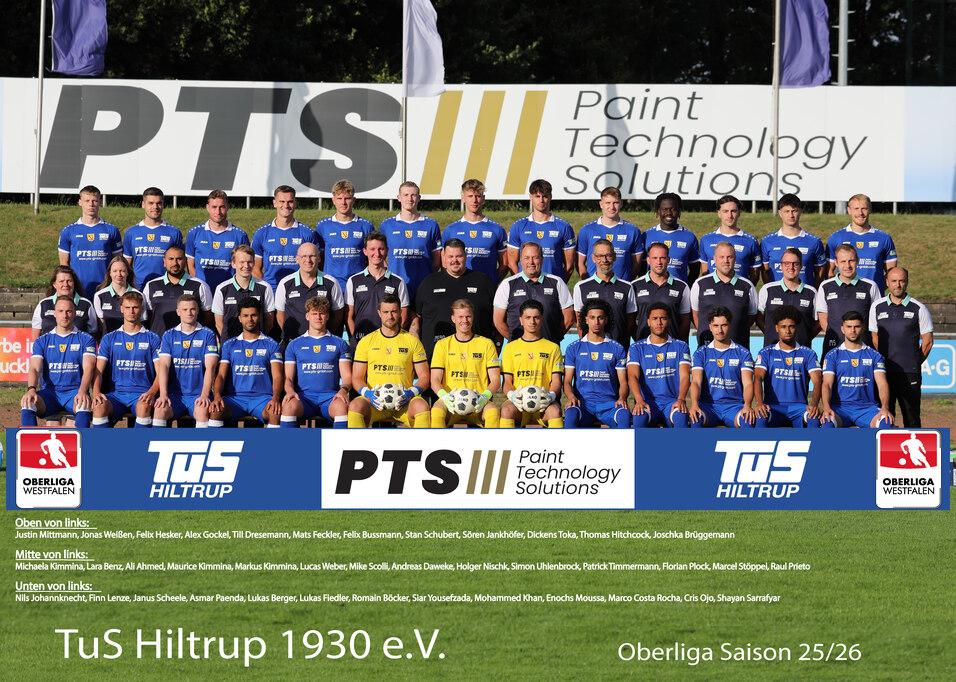 Mannschaftsfoto des TuS Hiltrup 1930 e.V. in blauen Trikots auf einem Fußballplatz, mit Banner im Hintergrund.