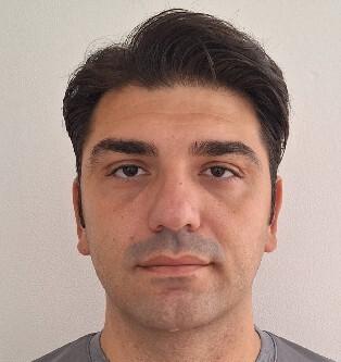 Porträt eines Mannes mit kurzen, dunklen Haaren, der ein graues T-Shirt trägt, vor einer neutralen Wand.