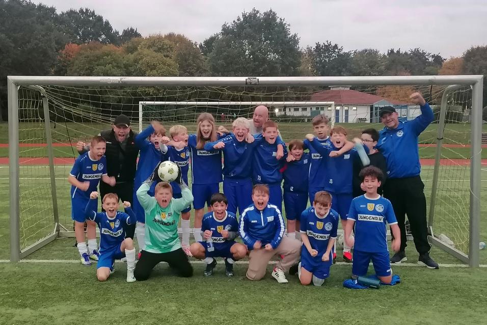Gruppe von jubelnden jungen Fußballspielern in blauen Trikots, stehend vor einem Tor auf einem Sportplatz.