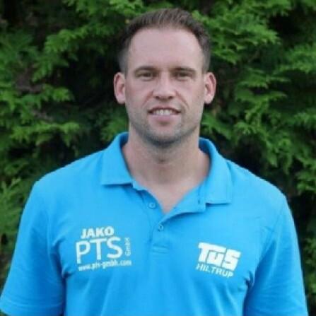 Portrait eines Mannes in blauem Polo-Shirt vor grünem Hintergrund, lächelnd und mit kurzen Haaren.