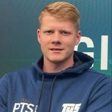 Porträt eines Mannes mit blonden Haaren, der in einem blauen Hoodie vor einer grünen Wand steht.