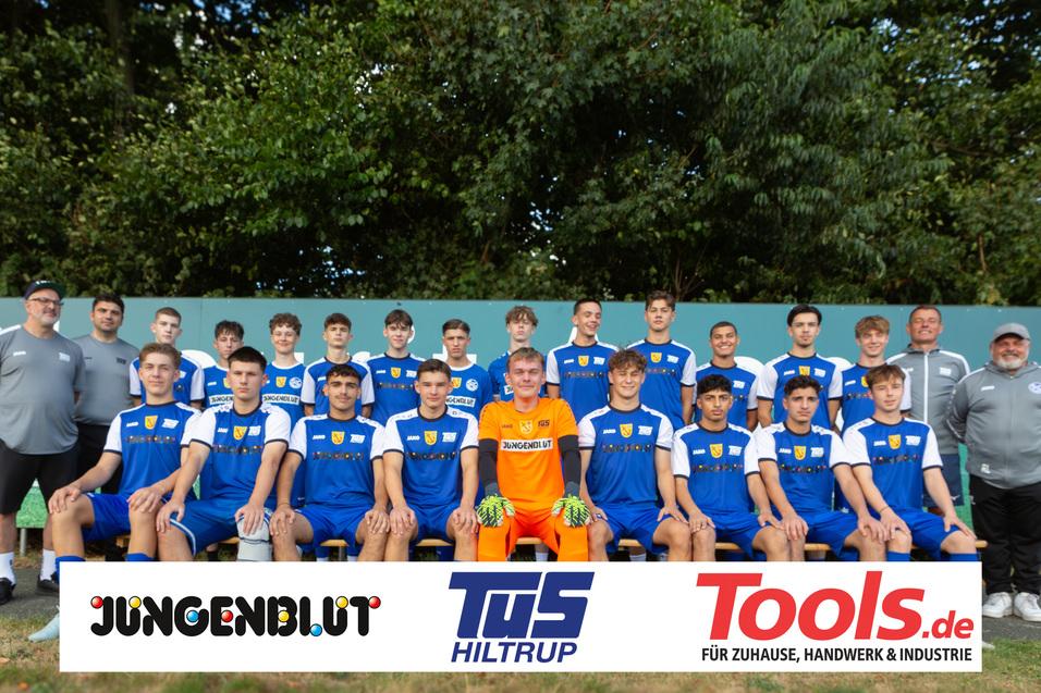 Mannschaftsbild einer Jugendfußballmannschaft in blauen Trikots mit Sponsorenlogos, auf einem Sportplatz.