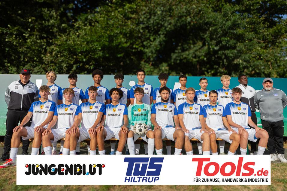 Mannschaftsfoto einer Fußballmannschaft in weißen Trikots mit blauen Akzenten, gefondet von Sponsorenlogos.