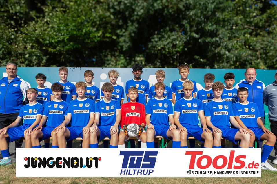 Mannschaftsbild einer Fußballjugendmannschaft in blauen Trikots, mit Trainer, auf einer Bank im Freien.