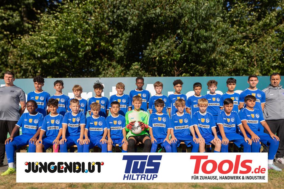 Mannschaftsfoto einer Jugend-Fußballmannschaft in blauen Trikots, begleitet von zwei Trainern im Hintergrund.