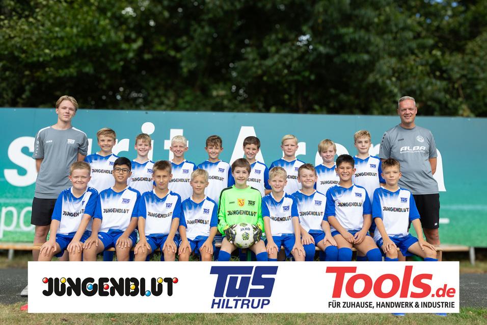 Mannschaftsfoto einer Jugend-Fussballmannschaft mit Trainer, alle tragen blaue Trikots auf einem Platz.