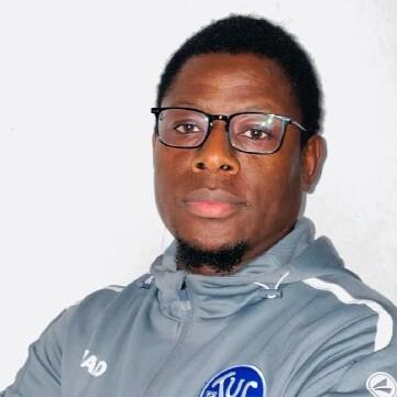 Porträt eines Mannes mit Brille in grauem Sportanzug, der mit verschränkten Armen in die Kamera schaut.