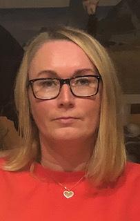 Frau mit kurzen blonden Haaren und Brille, trägt ein rotes Shirt und schaut direkt in die Kamera.