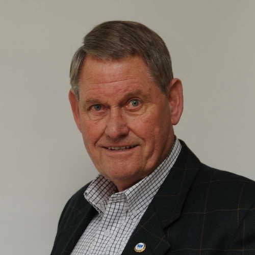 Porträt eines älteren Mannes mit kurzen grauen Haaren, in einem karierten Blazer und einem gestreiften Hemd.