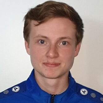 Porträt eines jungen Mannes in einem blauen Sportjackett mit Logos, vor einem neutralen Hintergrund.