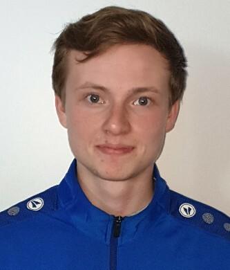 Porträt eines jungen Mannes in einem blauen Sportjackett mit Logo auf dem Rücken, vor einem neutralen Hintergrund.