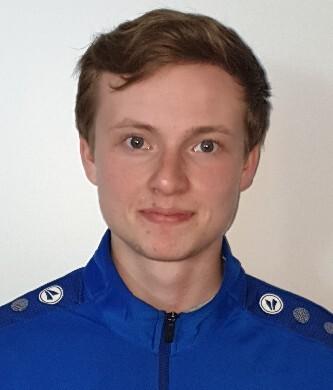 Portr&auml;t eines jungen Mannes in einem blauen Sportjackett mit Logo auf dem R&uuml;cken, vor einem neutralen Hintergrund.