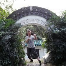 Mann steht unter einem geschmückten Torbogen, umgeben von Pflanzen, mit einer kämpferischen Pose.