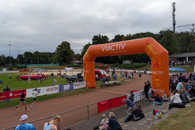 Läufer passieren einen großen orangen Zieleinlauf von "VIACTIV" bei einer Sportveranstaltung mit Zuschauern.