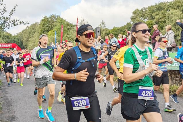 Gruppe von Läufern in Sportkleidung während eines Wettlaufs auf einer asphaltierten Strecke, umgeben von Zuschauern.