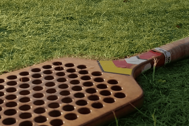 Holzschläger mit Löchern liegt auf frischem, grünem Gras.