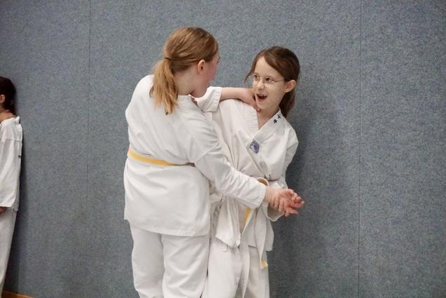 Zwei Kinder im Karateanzug interagieren spielerisch an einer Wand im Trainingsraum.